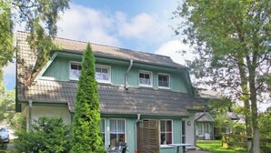 A two-story house with a green exterior, a sloped roof, and a front porch with a table and chairs.