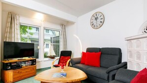 A living room with a sofa, a wooden coffee table, a TV on a wooden stand, and a clock on the wall.