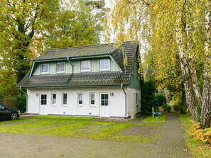 Ein zweistöckiges Haus mit grünem Dach und weißen Wänden, einem gepflasterten Einfahrt und einem von Bäumen gesäumten Weg.