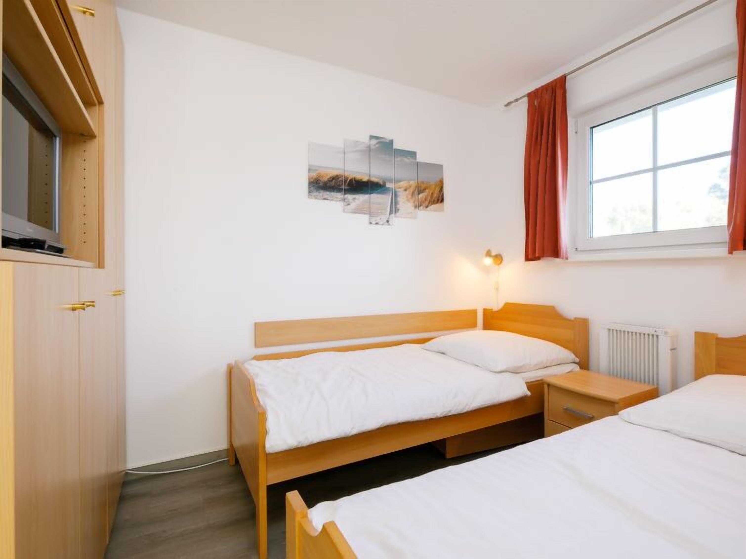 A hotel room with two wooden beds, a wall-mounted TV, a radiator, and a window with curtains.