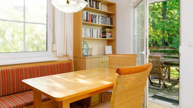 A cozy dining area with a wooden table and bench, a bookshelf, and a view of a garden through a glass door. - Im Kiefernweg DHH 21 by Interhome (Zinnowitz)
