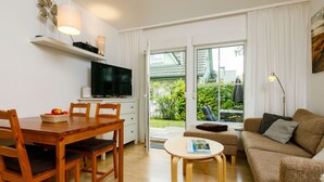En moderne stue med et træspisebord, stole, en sofa, et fjernsyn og et lille bord med et magasin.