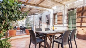 Eine Terrassengruppe im Freien mit einem Holztisch und -stühlen, umgeben von Blumentöpfen und einer Pergola.