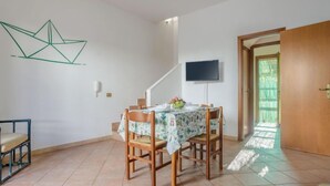 Ein Essbereich mit einem Tisch für vier Personen, einem Stuhl, einem an der Wand montierten Fernseher und einer zur Außenseite führenden Tür.