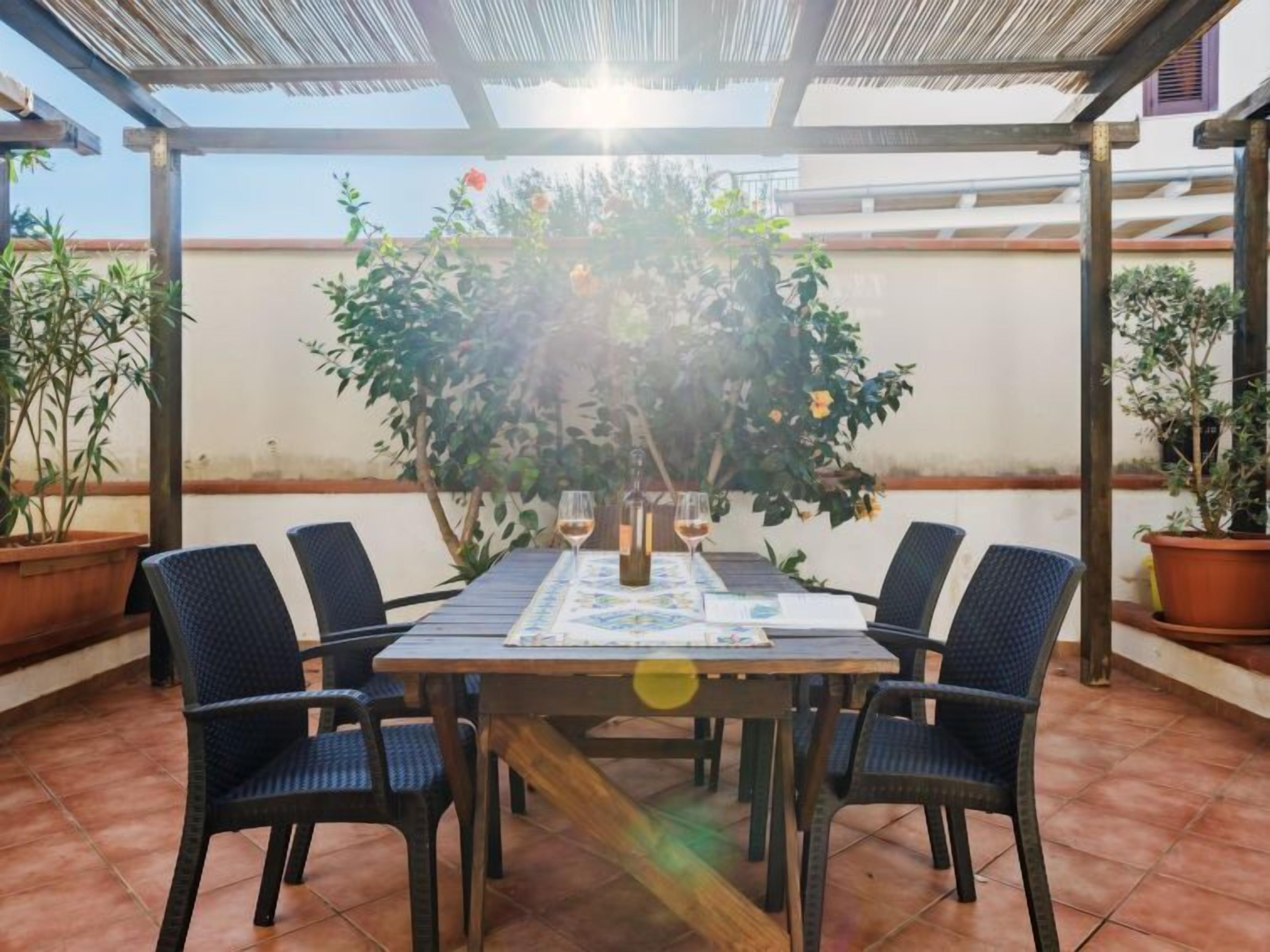 Eine überdachte Terrasse im Freien mit einem runden Tisch und sechs Stühlen, umgeben von Blumentöpfen.