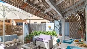Um pátio externo com móveis de vime, uma mesa posta para refeições e uma área coberta com telhado de bambu.