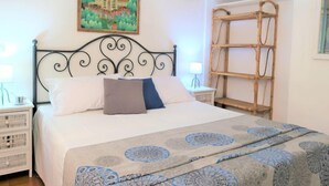 Cama bem arrumada com colcha estampada, cabeceira com design decorativo, mesa de cabeceira com abajur e um quadro de um edifício tradicional na parede.