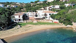 Uma área residencial costeira com casas numa encosta, praia clara e piscina.