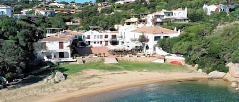 A coastal residential area with houses on a hillside, a clear beach, and a swimming pool.
