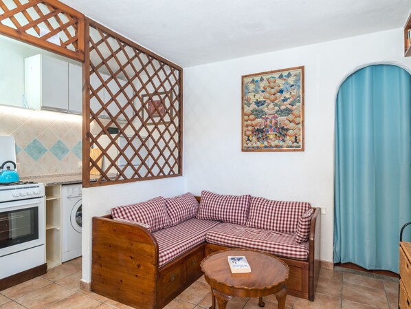 Un espacio de sala acogedor con un sofá a cuadros, una mesa de centro de madera y una cocina al fondo.