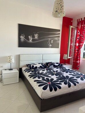 Une chambre à coucher moderne avec un grand lit, une table de chevet, une lampe, un tableau décoratif au mur et des rideaux rouges.
