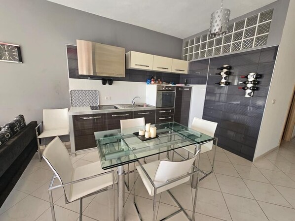 Une cuisine moderne avec une table à manger en verre, des chaises blanches et un meuble à vin.