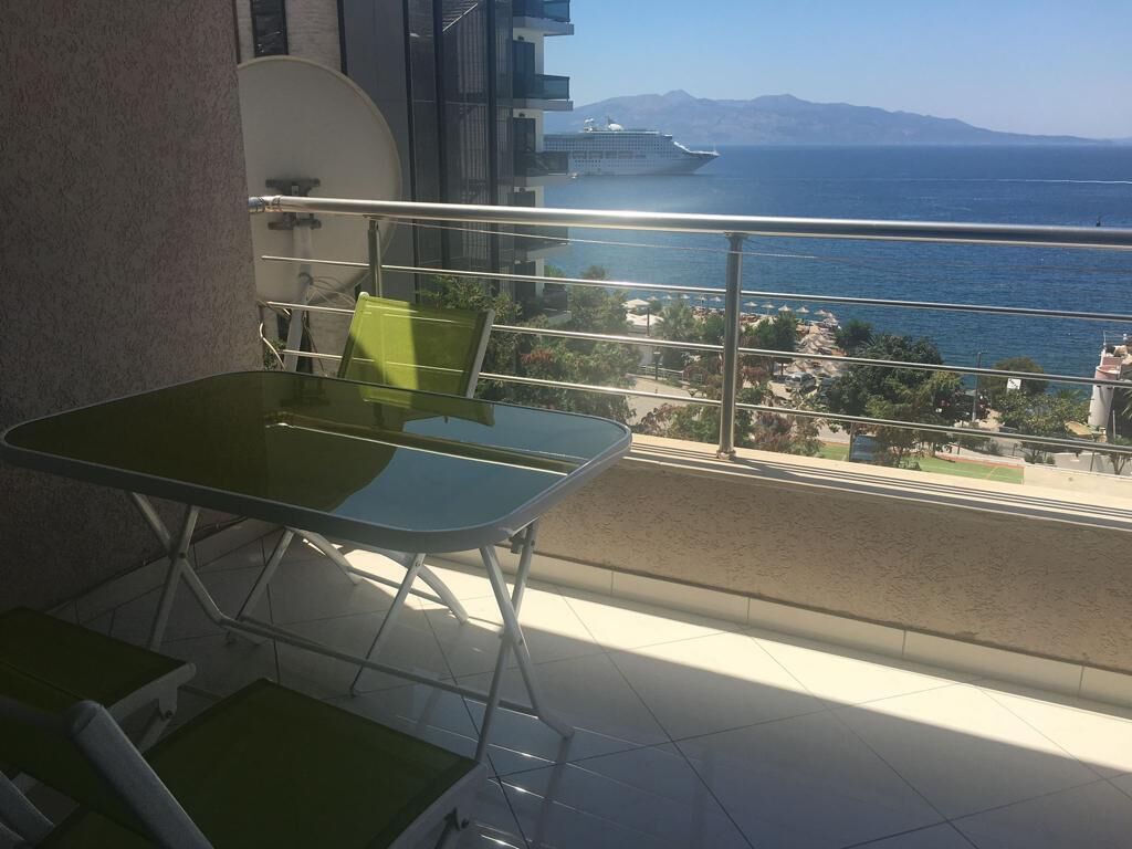 Un balcon avec une table et des chaises, une vue sur la mer et un navire de croisière à l’horizon.