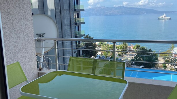 A balcony with a table and chairs, overlooking a body of water and a distant mountain range. - Appartamento in centro con vista e garage (Sarandë)