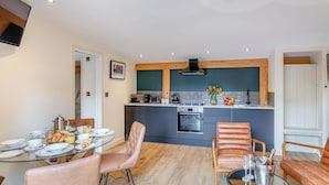 A modern kitchen with a central island, a dining area with a glass table, and a seating area with leather chairs. - 2 bedroom accommodation in Llagadfan, Welshpool (Llagadfan, Welshpool)