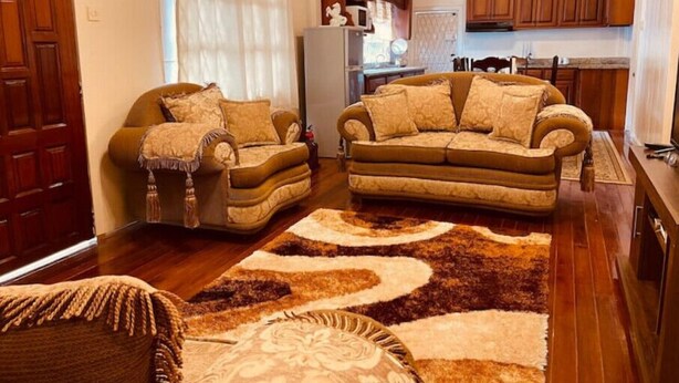 A living room with two sofas, a coffee table, and a patterned rug. There is a kitchen in the background with wooden cabinets and a refrigerator. - Upper flat in Eccles Home, 3 bedrooms, sleeps 6, AC, Hot Water (Georgetown)