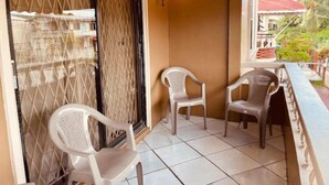 A balcony with two white plastic chairs, a tiled floor, and a view of greenery outside. - Upper flat in Eccles Home, 3 bedrooms, sleeps 6, AC, Hot Water (Georgetown)