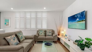 A living room with two sofas, a coffee table, a TV, and a window with blinds.