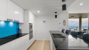 A modern kitchen with white cabinets, a blue countertop, and a view of the ocean.