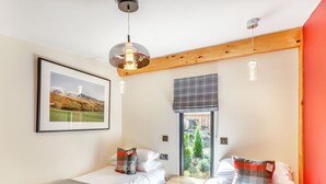 Ein Schlafzimmer mit zwei Betten, einem Fenster mit Blick auf Grünflächen, einem gerahmten Bild an der Wand und einer Deckenleuchte.