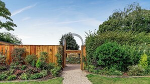 Ein Gartenweg, der zu einer hölzernen Struktur mit einem Metallbogen führt.