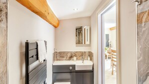 Ein modernes Badezimmer mit sichtbarem Holzbalken, einem schwarzen Waschtisch und einer weißen Spüle sowie einer Marmor-Spritzschutzwand.