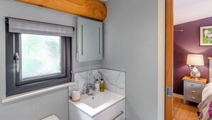 Un baño con ventana, un lavabo blanco, un espejo y una viga de techo de madera.