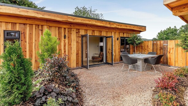 Una cabaña de madera con un patio de grava, una mesa de comedor y sillas.