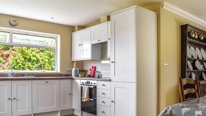 Een compacte keuken met witte kasten, een ingebouwde oven en een raam met uitzicht op groen.