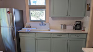 A kitchen with a stainless steel refrigerator, a sink with a window above, and light green cabinets. - Da Princess Inn - Walk to Downtown (Lafayette)
