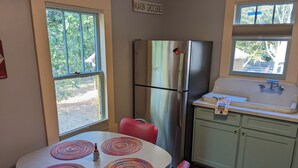 A compact kitchen with a refrigerator, sink, and a dining table with colorful placemats. - Da Princess Inn - Walk to Downtown (Lafayette)