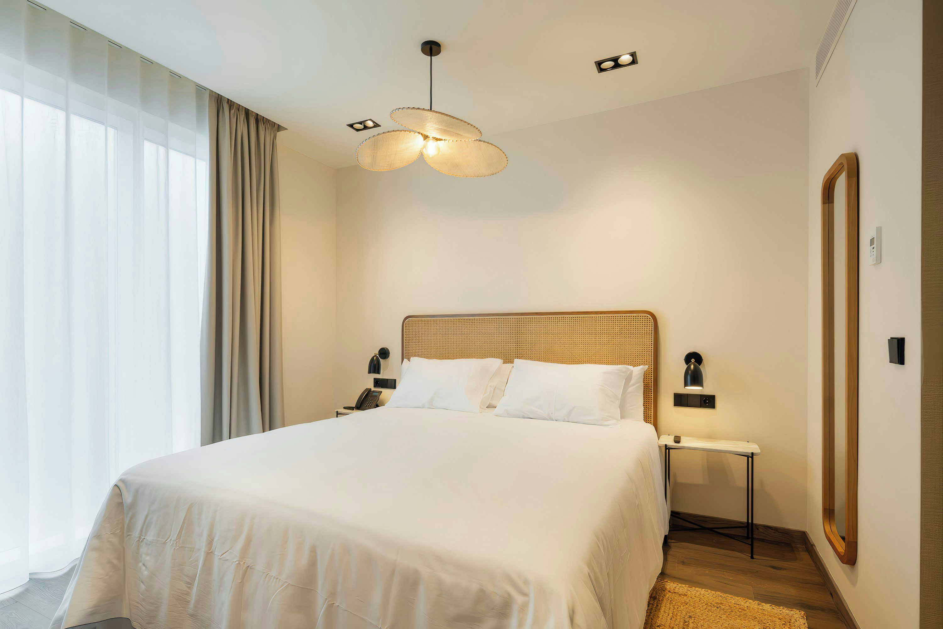 A hotel room with a large bed, a bedside table with a lamp, a wall-mounted phone, and a mirror.