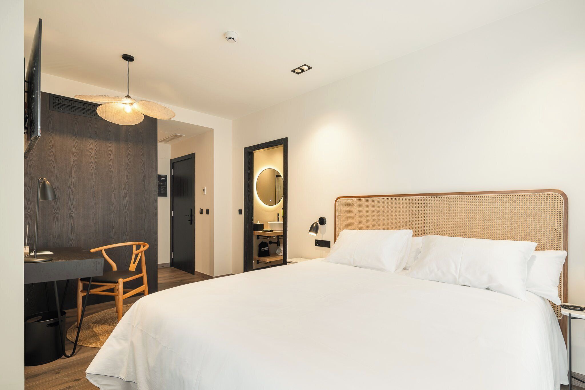 Habitación de hotel moderna con una cama grande, un escritorio con silla, un baño pequeño y un ventilador de techo.