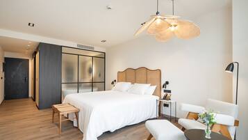 Un dormitorio moderno con una cama grande, un cabecero de madera, una mesita de noche, una silla, una lámpara de pie y un jarrón decorativo.