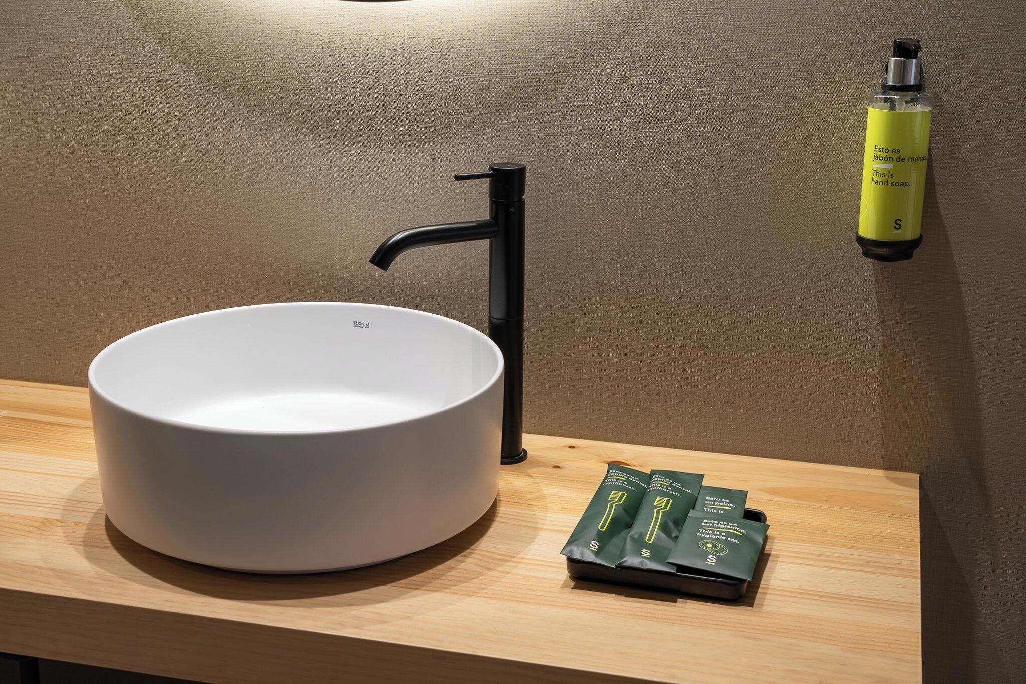 Ein modernes Badezimmer mit einem weißen Waschbecken, einem schwarzen Wasserhahn und einer Handseifenflasche an der Wand.