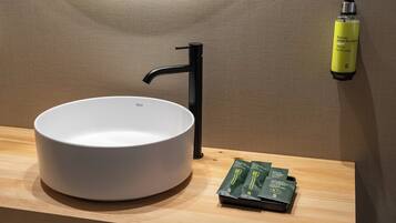 Ein modernes Badezimmer mit einem weißen Waschbecken, einem schwarzen Wasserhahn und einer Handseifenflasche an der Wand.