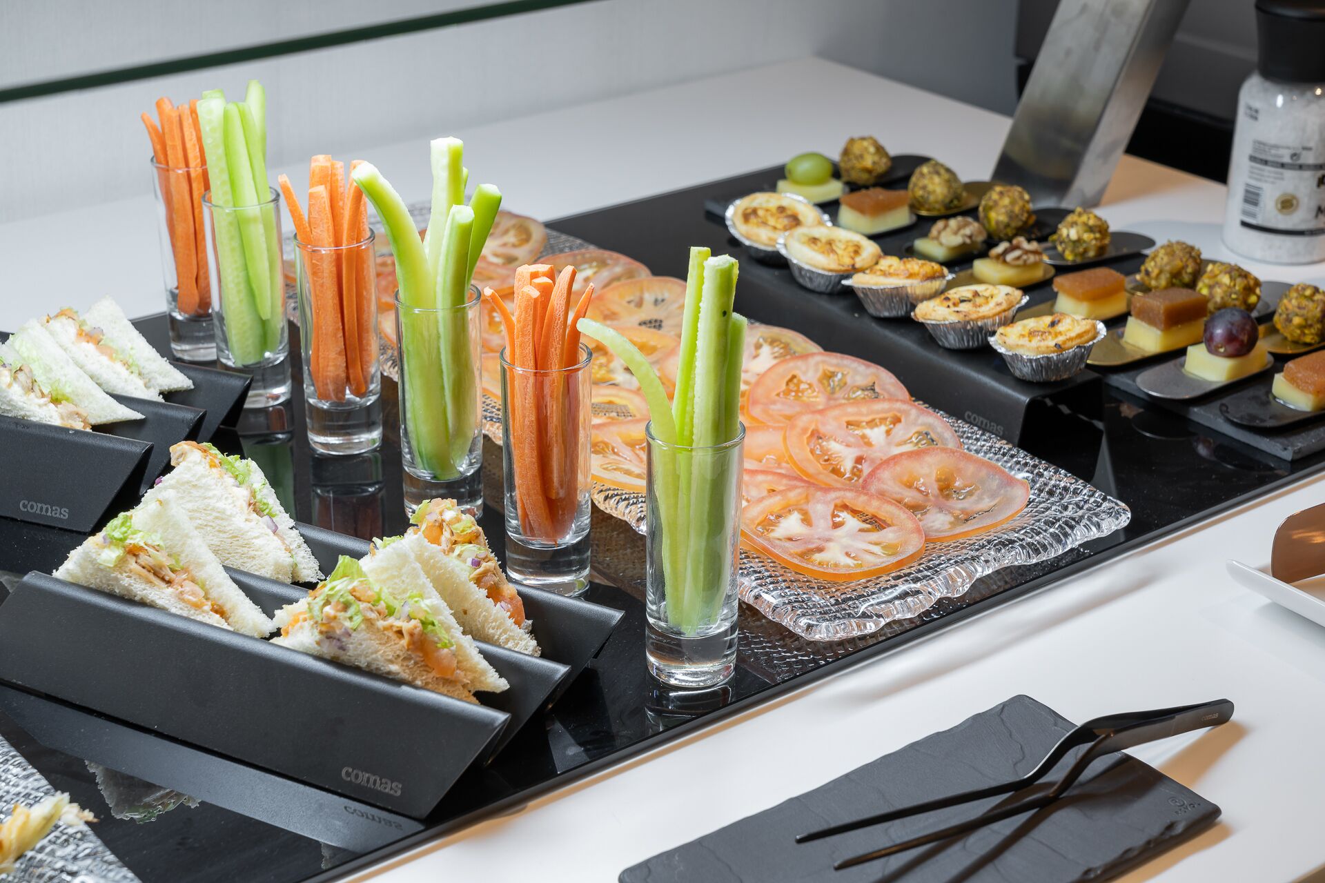 Una mesa de buffet con diversos alimentos, incluyendo sándwiches, palitos de apio y una variedad de pasteles.