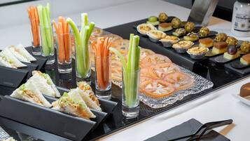 Una mesa de buffet con diversos alimentos, incluyendo sándwiches, palitos de apio y una variedad de pasteles.