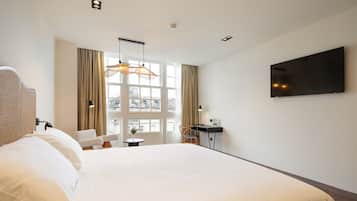 Habitación de hotel con una cama grande, un escritorio con silla, televisor montado en la pared y una ventana con cortinas.
