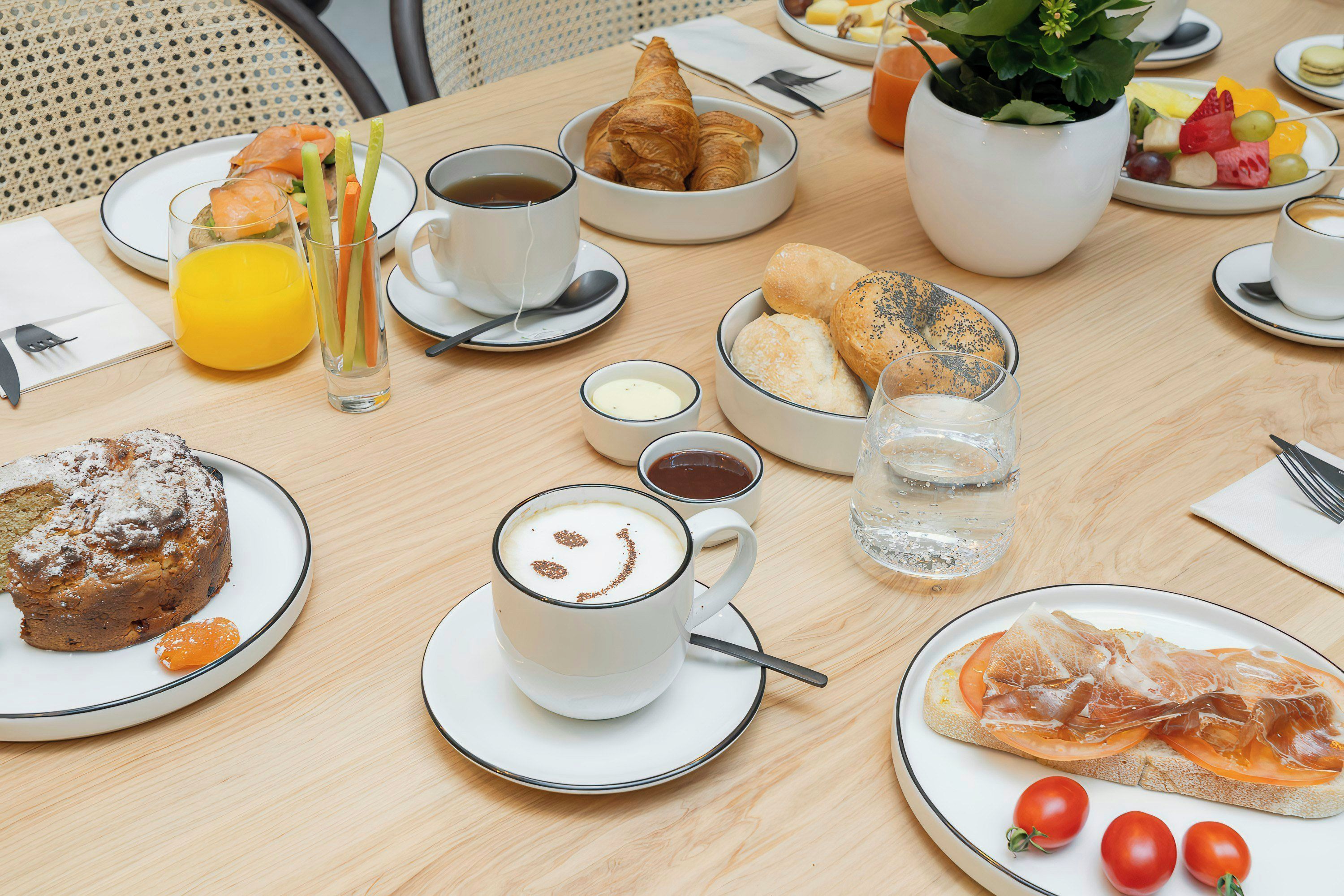 Una mesa de desayuno con cruasanes, bollería, fruta y café.
