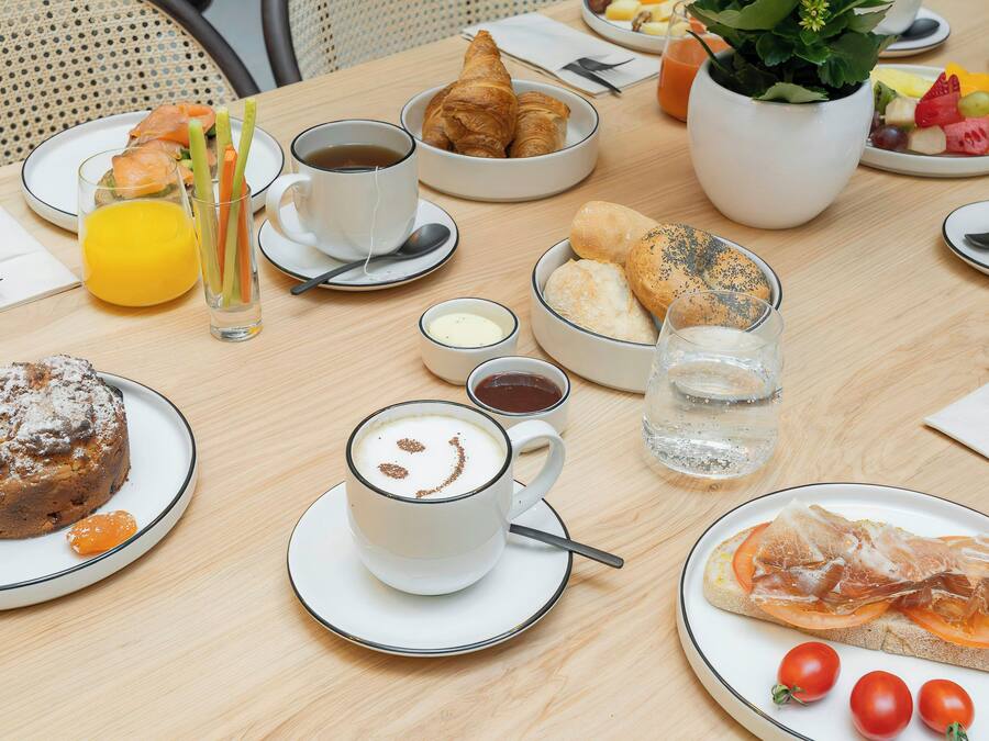 Una mesa de desayuno con cruasanes, bollería, fruta y café.