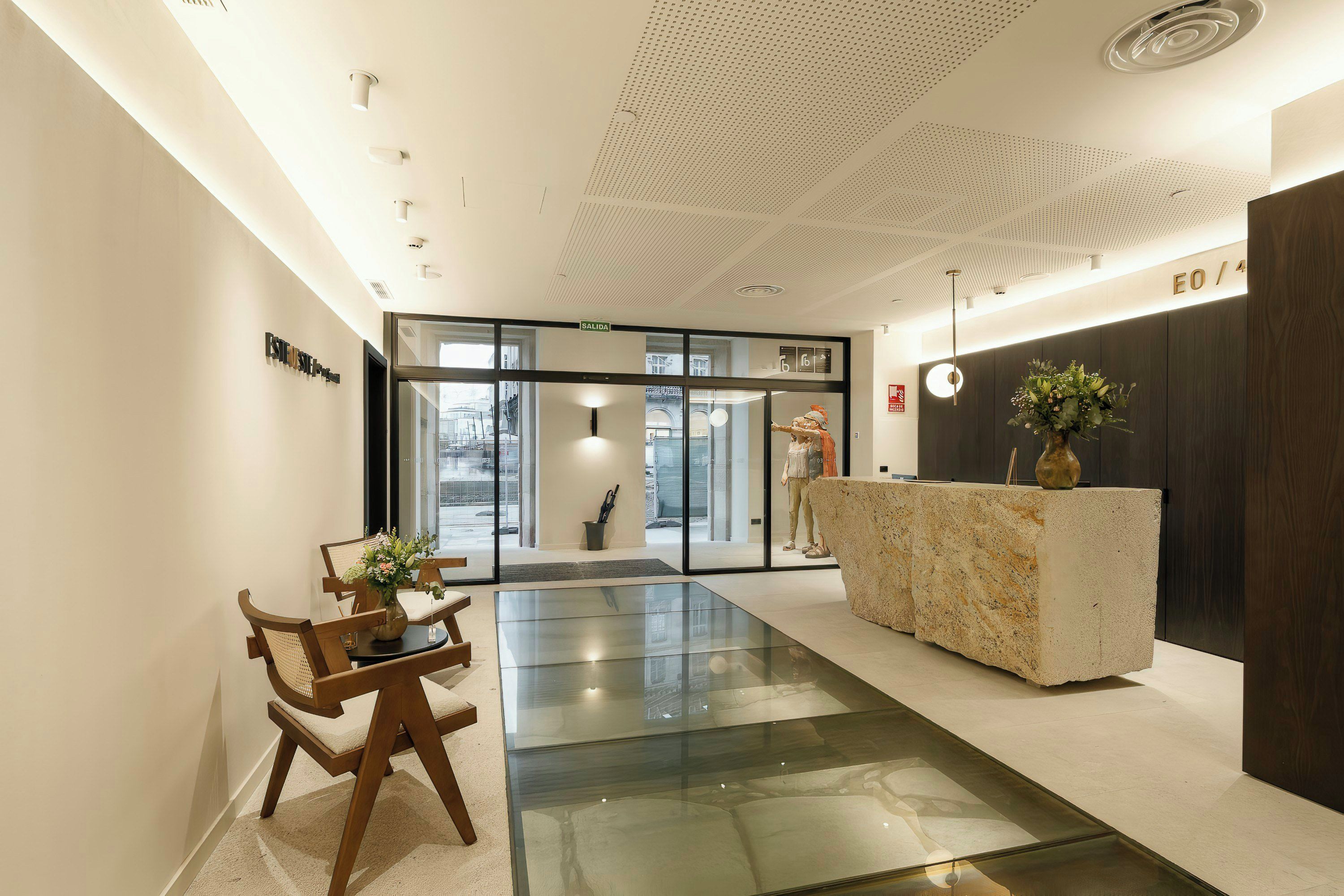 A modern reception area with a glass partition, a reception desk, and a seating area with a table and chairs.