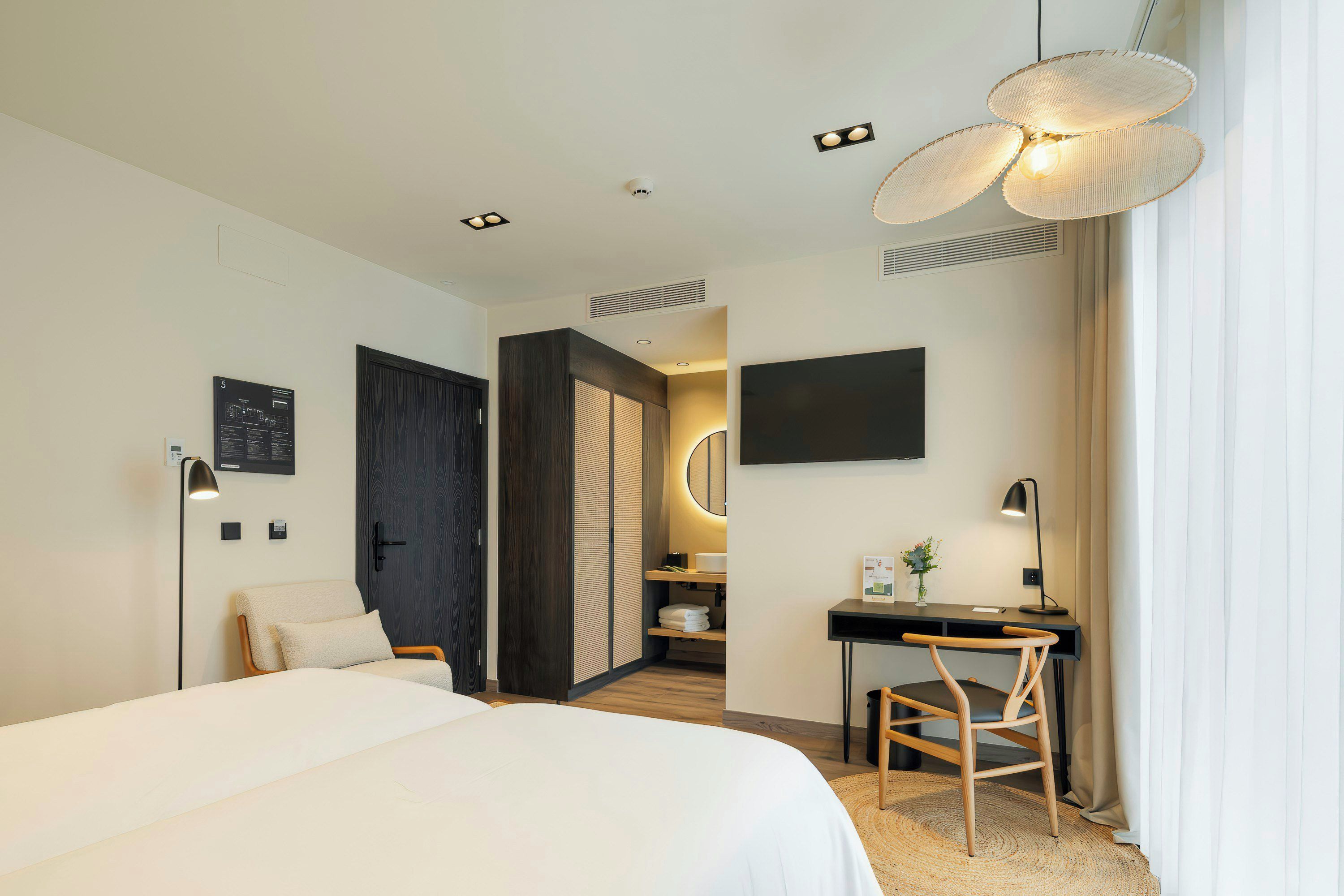 A modern hotel room with a bed, desk, chair, and a large window.