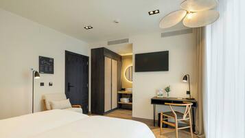 A modern hotel room with a bed, desk, chair, and a large window.
