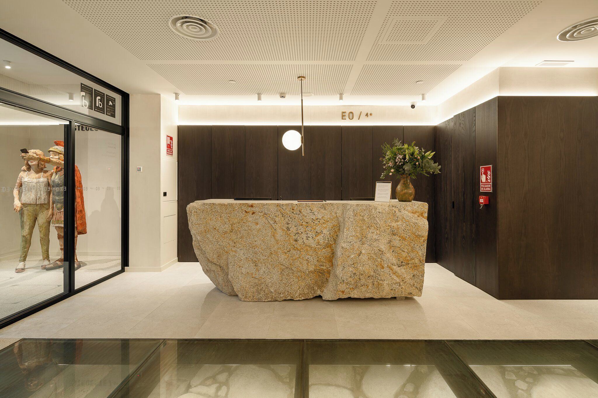 A reception area with a large, textured stone counter, a glass display case with mannequins, and a modern ceiling design.