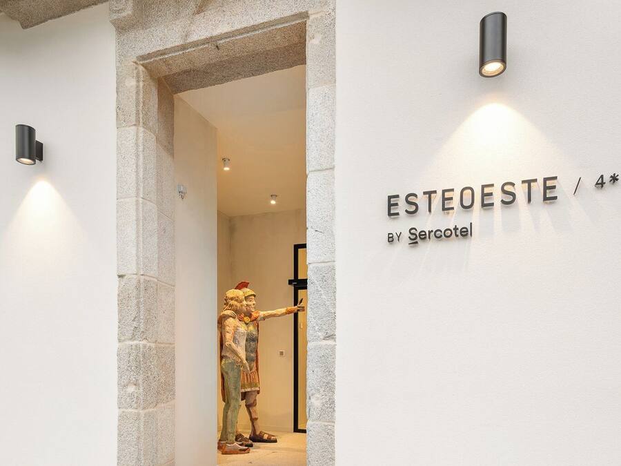 A hotel entrance with a stone facade, a mannequin dressed in traditional attire, and a sign reading "ESTEOESTE BY Sercotel".
