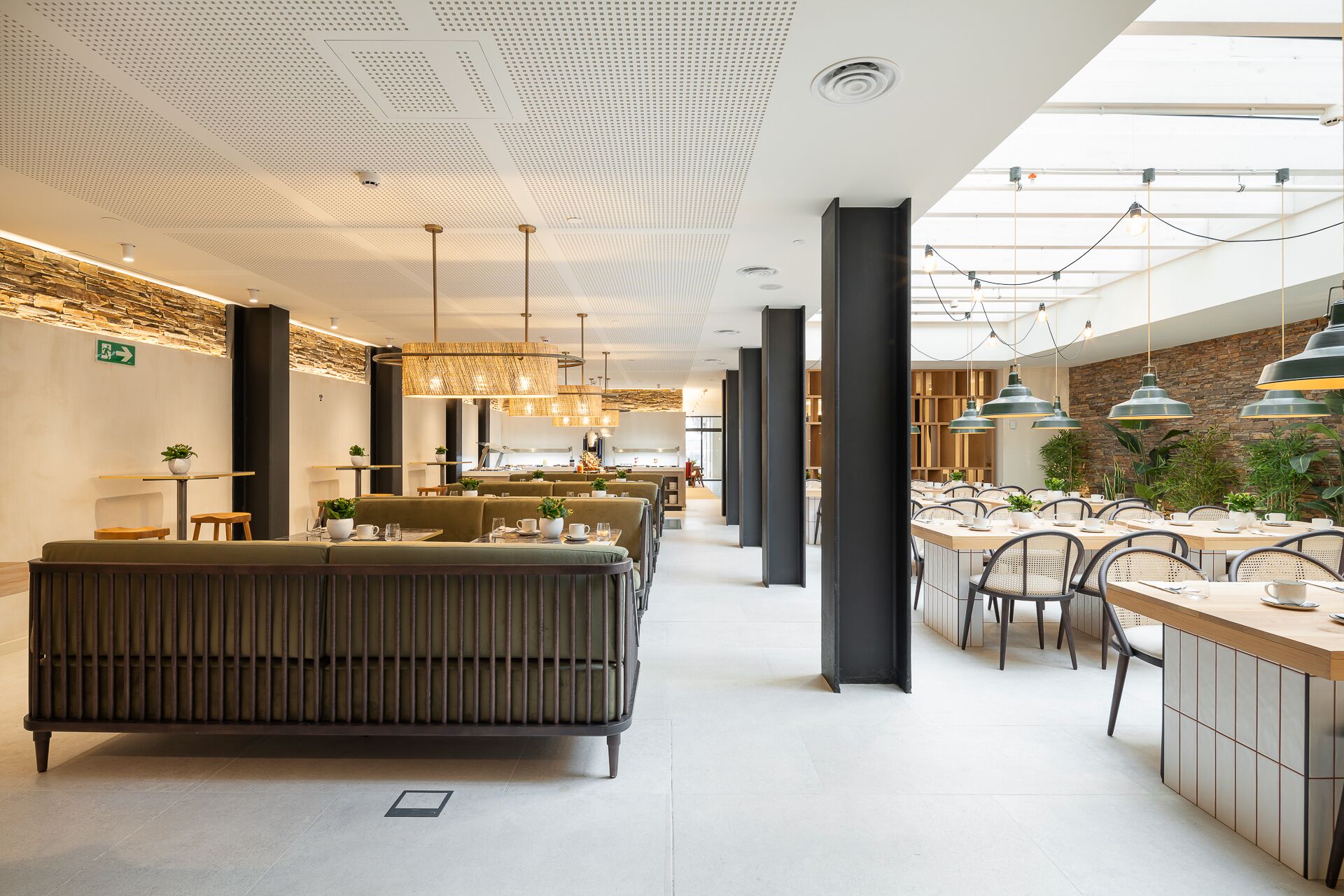 A modern restaurant with a central seating area, high ceilings with perforated panels, and pendant lighting.
