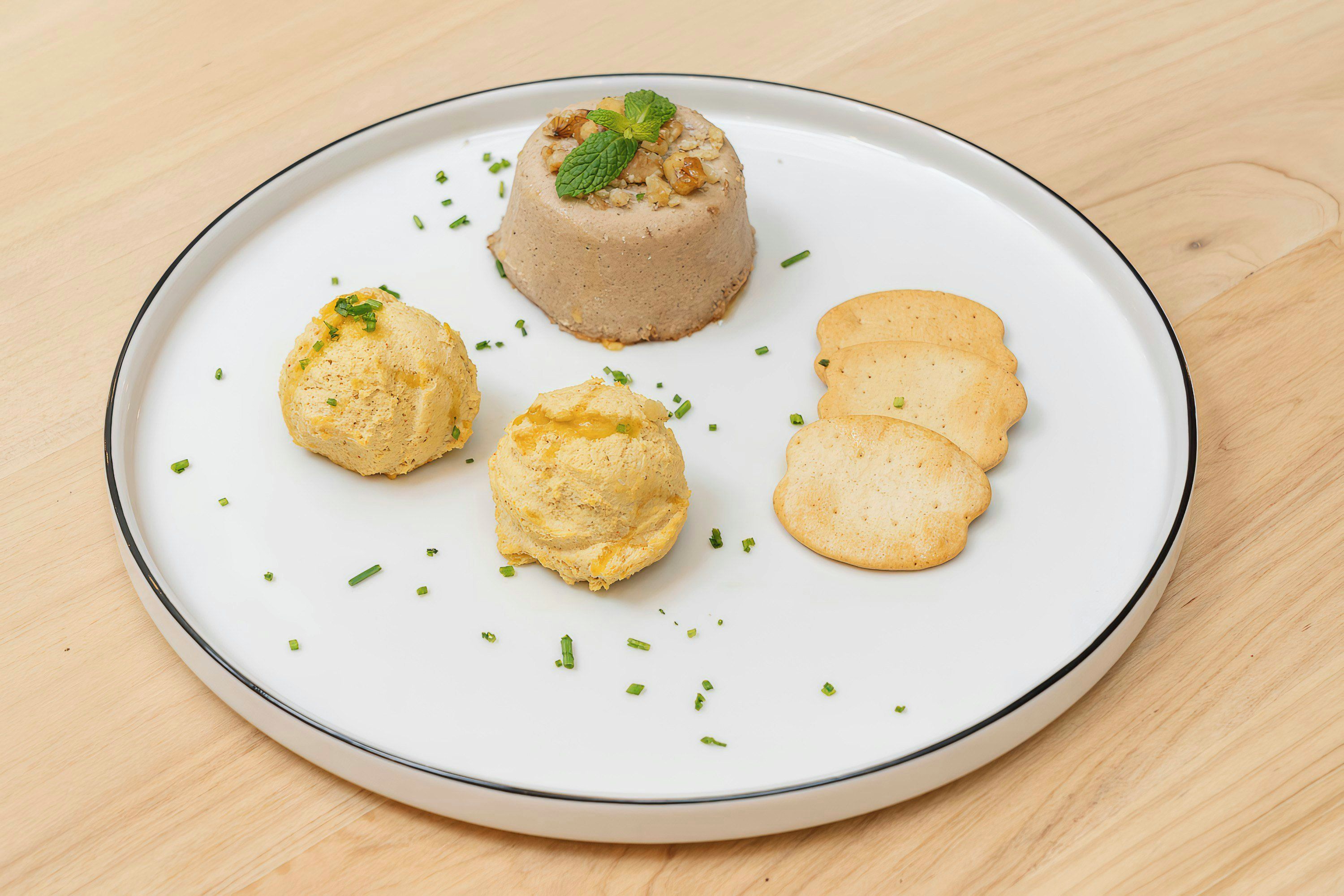 A plate with a dessert consisting of a round cake topped with nuts and a mint leaf, accompanied by three round pastries and four round biscuits.