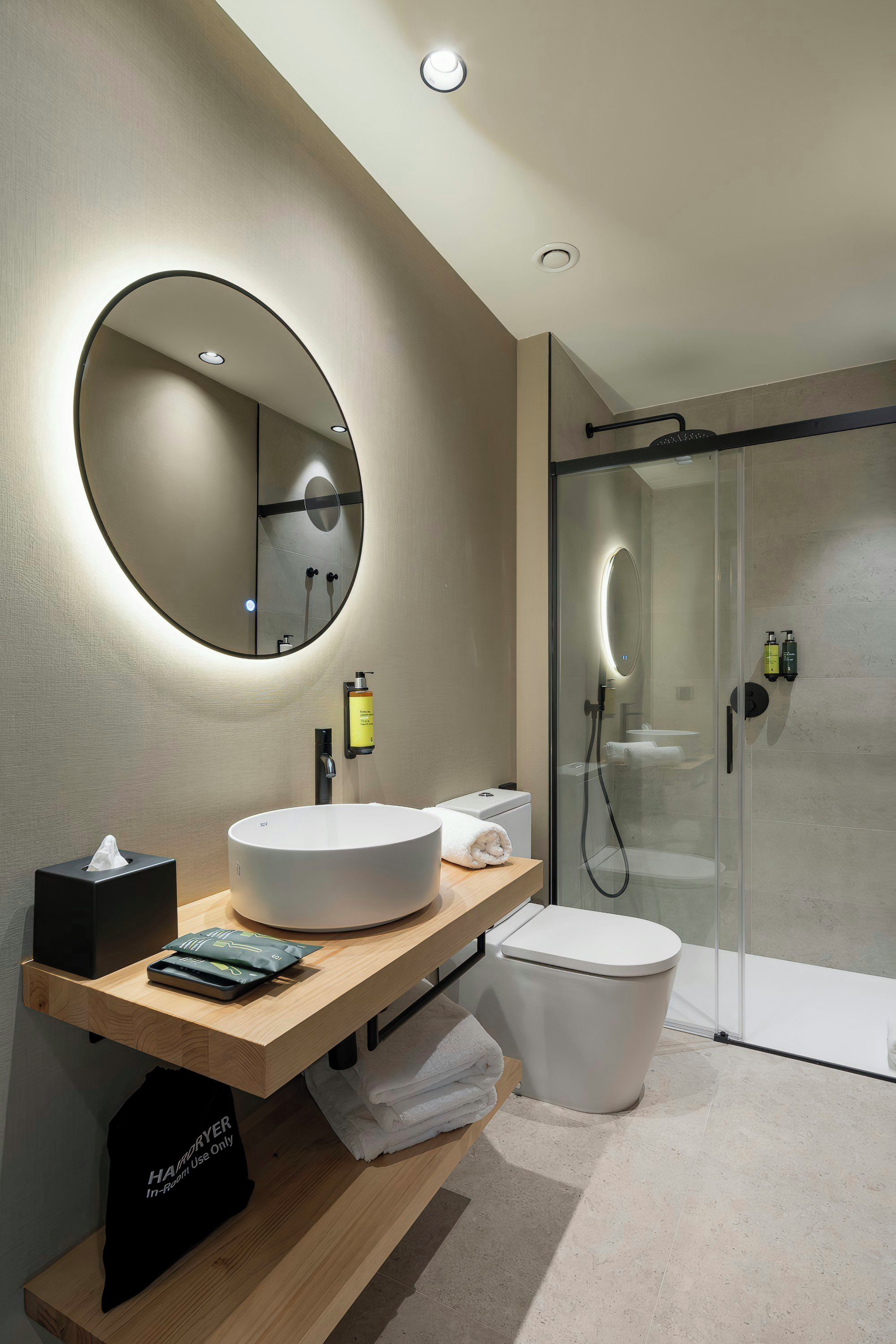 A modern bathroom with a round mirror, a sink, a toilet, and a glass-enclosed shower.