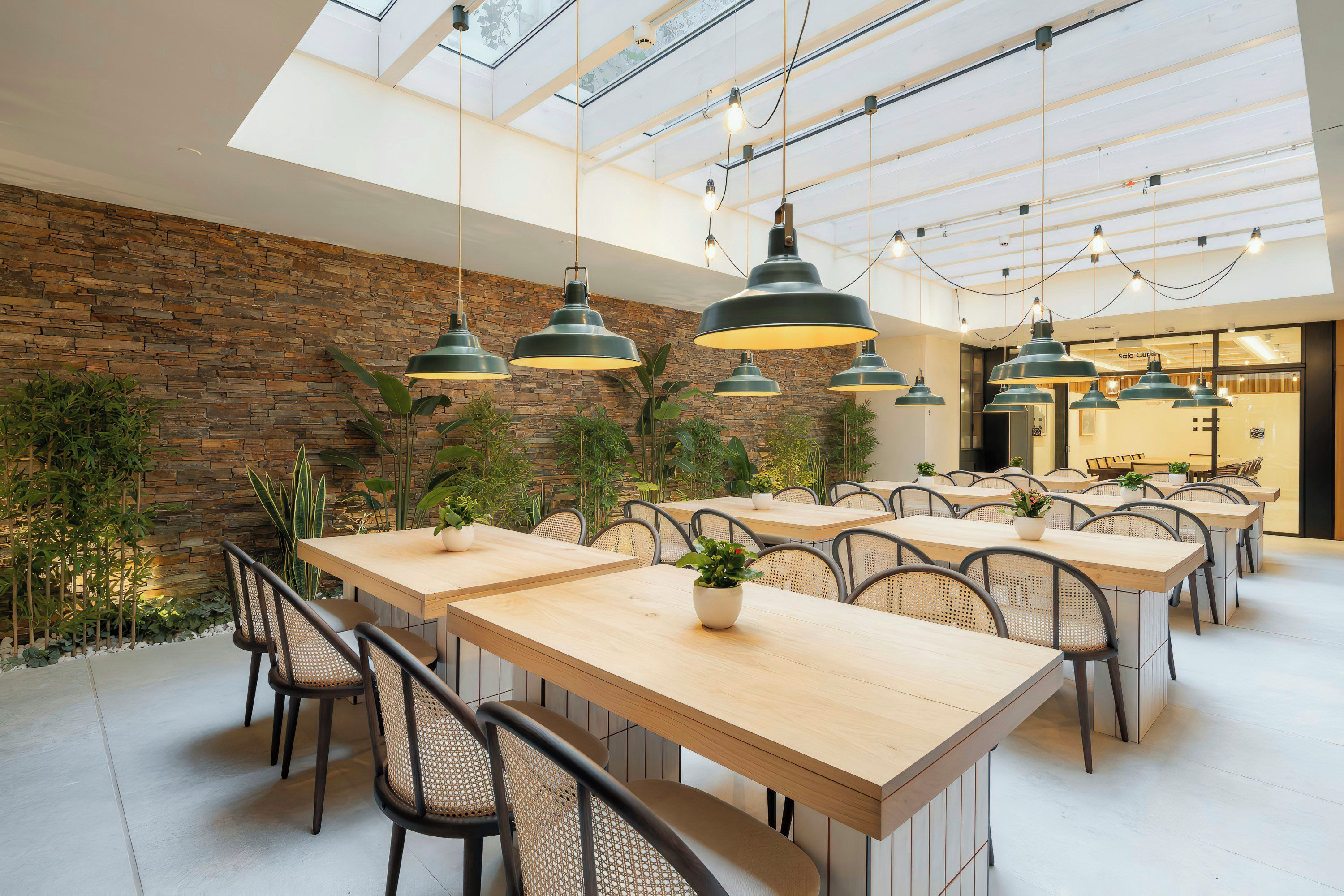 A modern dining area with multiple tables and chairs, a stone wall, and hanging pendant lights.